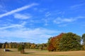 Landscape in Bavaria in autumn, with colorful trees, fields and a wooden house, in front of a blue sky with clouds