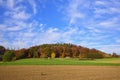 Landscape in Bavaria in autumn, with colorful trees, fields and a wooden house, in front of a blue sky with clouds