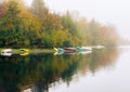 Landscape of boats on the shore of a lake surrounded by a forest covered in the fog in autumn Royalty Free Stock Photo