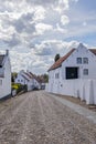 Landscape of cobbled street between houses with white walls against blue sky covered with clouds Royalty Free Stock Photo