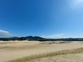 Landscape composed of sand dunes with grass against vegetation in the background, a city, green mountains and the sea under the Royalty Free Stock Photo