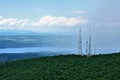 Landscape with green hills with body of water river maybe in the background. Far rain or mist and cellphone tower aside. Royalty Free Stock Photo