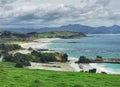 Landscape image of an ocean beach with dunes and cliffs under cloudy sky