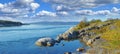 Landscape of a lake with a rocky shore on a bright cloudy day. Green hill with boulders by the seaside with a blue sky