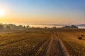 Landscape of a large hilly harvested agricultural wheat field with straw bales at sunrise. Beyond the field is a misty valley and Royalty Free Stock Photo