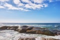 Landscape of large rocks in the ocean with a cloudy blue sky and copy space. Sea waves splashing against boulders on Royalty Free Stock Photo