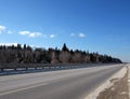 Landscape with empty suburban highway with metal a fence on the sides and forest under blue sky on sunny winter day