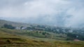 Landscape with a mountain village and fields with flowers on a cloudy summer day after rain with a haze