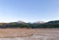 Landscape with mountains, snoe peaks and green hills. Dry cracked earth. Drought. The dried-up bottom of the river