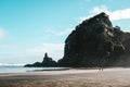 Landscape of the Piha beach and high rocks with the people walking around it under a blue sky