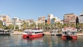 Landscape of the port of Alicante full of palm trees and buildings, two red ships ready to sail towards the island of Tabarca with