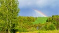 Landscape with a rainbow. A real rainbow in the cloudy sky after the rain in summer. Hilly countryside with a bright rainbow after