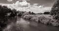 Landscape with a river next to a field and a farm with clouds in the background, black and white Royalty Free Stock Photo