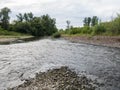 Landscape of river Ukrine, fast water current eroding gravel shore, riverbank overgrown with green bushes and trees during