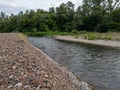 Landscape of river Ukrine, fast water current eroding gravel shore, riverbank overgrown with green bushes and trees during