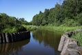 Landscape of a rivier with banks embanked with wooden logs. Sunny summer view. Royalty Free Stock Photo