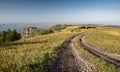 Landscape with a road in a field in the mountains with wildflowers and grass and a river in the background on a summer sunny day Royalty Free Stock Photo