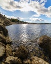 Landscape of rocks in a blue lake with sky with clouds and sun reflecting in the water. Royalty Free Stock Photo