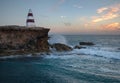 Landscape with rocky cape on the ocean with a small lighthouse at sunset