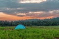 Camping tent on grass field with background of forest and mountains and sunrising sky in natural park Royalty Free Stock Photo