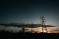 Landscape shot of metallic transmission towers with powerlines connecting them during sunset