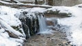 Landscape with a small waterfall and flooded water, frozen icicles, stones covered with green moss, ice and snow