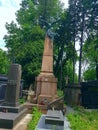 Landscape. A stone crypt of brown color. Above it is a dragon of green color. Around the other crypts, green grass and trees.