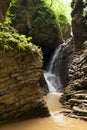 Landscape with summer stormy cascade waterfalls in canyon, lush green forest, sunbeams, splashes, layered rocks overgrow green.