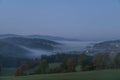 Landscape in the sunrise in the fog in the morning with meadow field forest tree mountains in the background near Grafenau in the