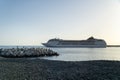 Liner boat leaving for a cruise in the sea with sunset light and pebble beach in first plan, Funchal, Madeira island, Portugal Royalty Free Stock Photo