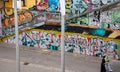 Landscape view of tourists passing graffiti & urban art lining the embankment walls of the \