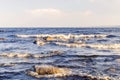 Landscape of the water surface of a large lake with stones and waves against the blue sky.