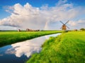 Landscape with windmill and rainbow. A huge cloud after a storm. Reflections on the surface of the water.