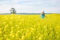 Landscape woman in blue dress and straw hat walk in yellow colza field