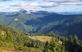 The landscape with the wooden hut and fence on the lawn with green fir trees, high mountains covered by forests, sky with clouds. Royalty Free Stock Photo