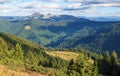 The landscape with the wooden hut and fence on the lawn with green fir trees, high mountains covered by forests, sky with clouds. Royalty Free Stock Photo