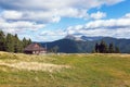 The landscape with the wooden hut and fence on the lawn with green fir trees, high mountains covered by forests, sky with clouds. Royalty Free Stock Photo