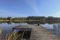 Landscape with wooden long jetty with chair for fishing, lake, forest on horizon and clear blue sky in summer Royalty Free Stock Photo