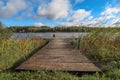 Landscape with wooden long jetty with chair for fishing, lake, forest on horizon and cloudy blue sky in summer Royalty Free Stock Photo