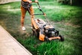 Landscaping concept - worker, gardener working with lawnmower and cutting grass in garden