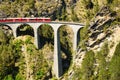 Landwasser viaduct in the Davos mountains near Filisur. Beautiful old stone bridge with a moving train. Spring Time