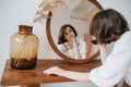 Languid woman in a white dress in front of the mirror