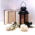 The lantern of Ramadan is black in color, luminous, decorated with wooden motifs, next to the Holy Quran, with a few white roses Royalty Free Stock Photo