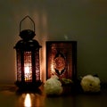 The lantern of Ramadan is black in color, luminous, decorated with wooden motifs, next to the Holy Quran, with a few white roses