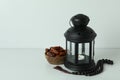 Lantern, rosary and bowl of dates on white background