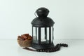 Lantern, rosary and bowl of dates on white background