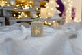 Lantern standing on white fabric. Festive Christmas and New Year decorations, garland lights, bokeh wooden fir on background. Royalty Free Stock Photo