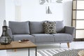 Lantern on table near grey sofa with patterned cushion in white