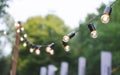 Lanterns-light bulbs on a background of green trees. Hanging lights at the festival. Street decor. Royalty Free Stock Photo