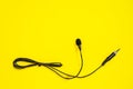 Lapel microphone with a bundled cord on yellow background, top view. Essential vlogging and journalism tools.